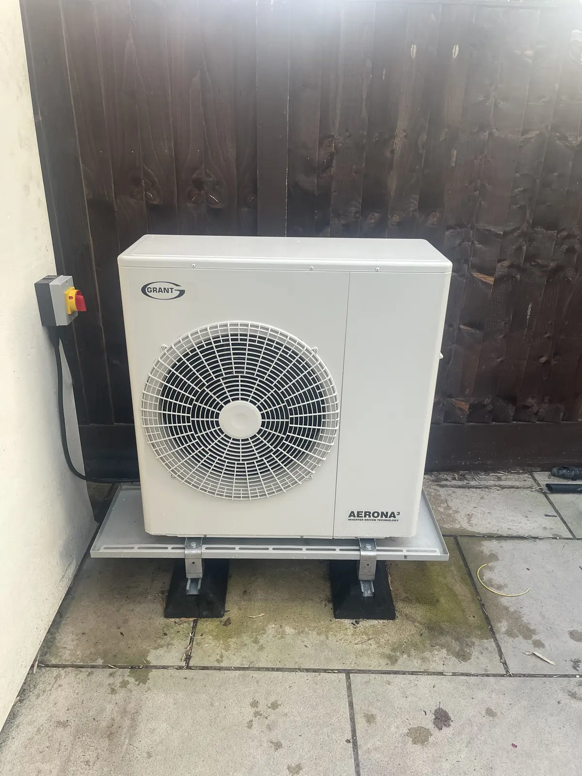 Grant Aerona3 air source heat pump outdoor unit on a stand beside a brick house